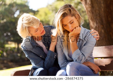 loving middle aged woman comforting her sad daughter at the park