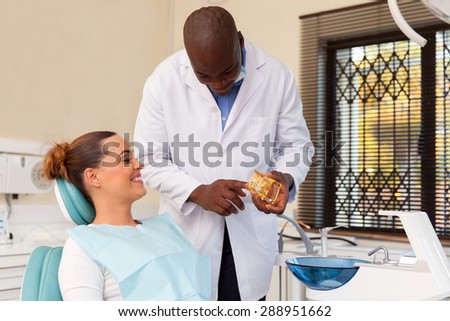 handsome african american dentist explaining teeth model to patient