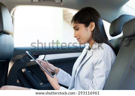 indian business woman using tablet pc in backseat of car