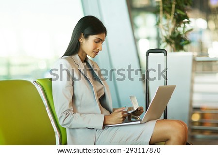 pretty indian businesswoman checking flight information on laptop computer at airport