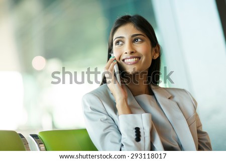 cheerful indian business woman talking on mobile phone at airport
