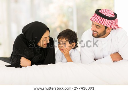 happy young muslim family of three lying on bed at home