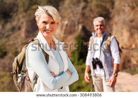 senior female hiker standing on mountain with husband on background