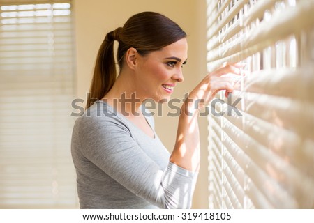 beautiful woman peeking through window blinds