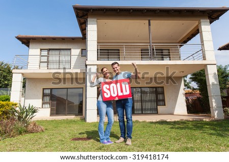 happy couple standing outside their house and holding sold sign