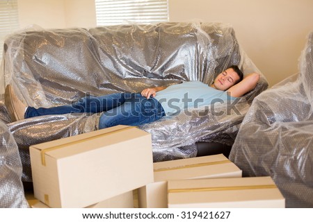 tired man sleeping on couch in new home with cardboard boxes around
