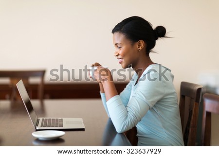 beautiful young african woman drinking coffee while using laptop at home