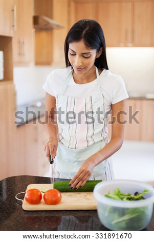beautiful indian woman chopping cucumber in home kitchen