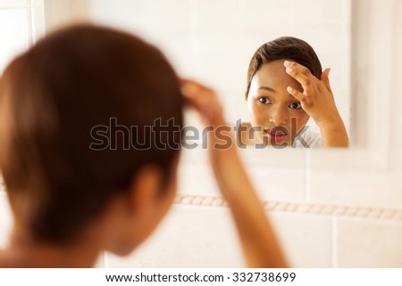 african girl checking her face for pimple looking in the mirror