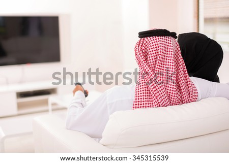 rear view of muslim couple watching tv at home