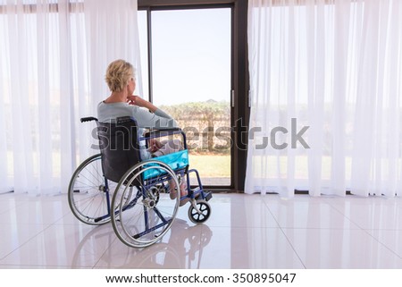 thoughtful disabled woman in wheelchair looking through door glass