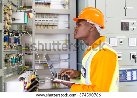 african industrial electrician working in power plant control panel