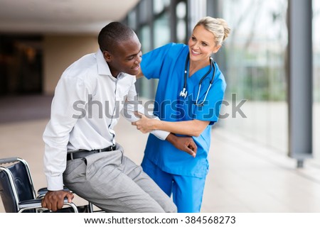friendly medical nurse helping handicapped man getting up from wheelchair