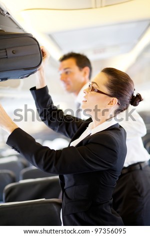 friendly flight attendant helping passenger with carry on luggage