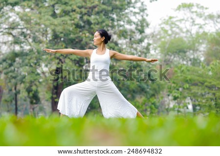 Beautiful woman practicing yoga in the park. Warrior Two/ Virabhadrasana II.