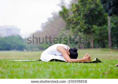 Beautiful woman practicing yoga in the park.Seated Forward Bend / Paschimottanasana.