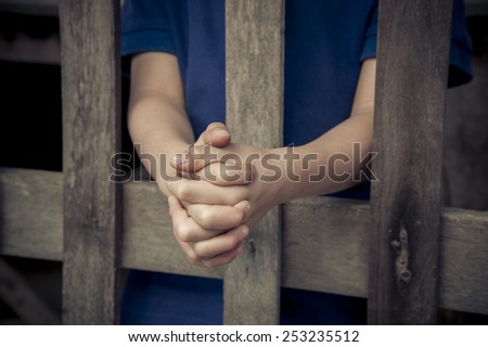 A boy standing behind a wood bar like jail