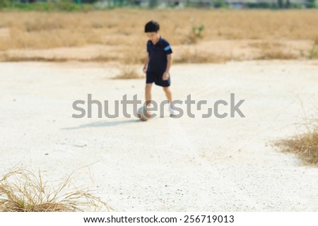 Out focus boy play football on dry soil ground in a shiny day