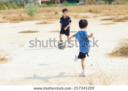 Boy play football on the dry soil ground in a shiny day