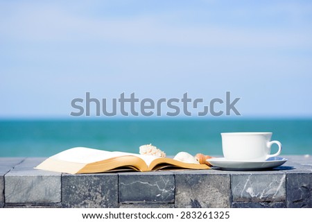 White coffee cup and old book on marble floor and sea sky background