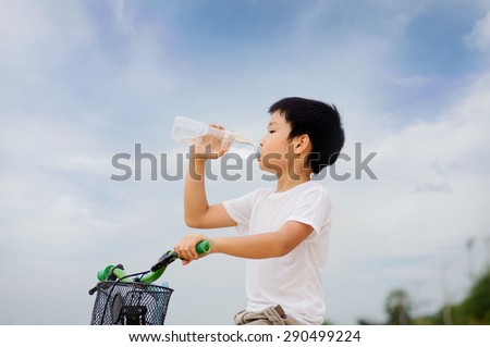 Asian young boy sit on bicycle  drinking fresh water from plastic bottle after sport in daylight