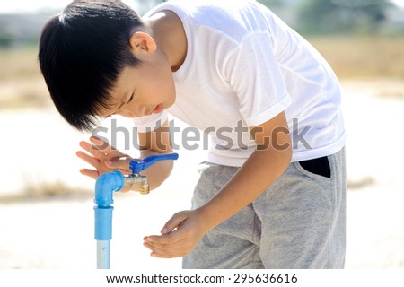 Close up Asian boy open metal blue water faucet on hot and dry empty land. Water shortage concept.