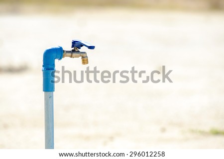Close up metal blue water faucet on dry land. Water shortage concept.