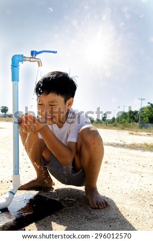 Close up Asian boy open metal blue water faucet on hot and dry empty land out focus the sun. Water shortage concept.
