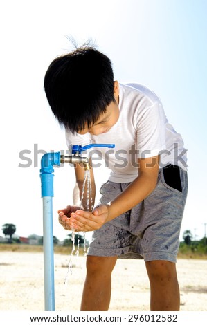 Close up Asian boy open metal blue water faucet on hot and dry empty land out focus the sun. Water shortage concept.