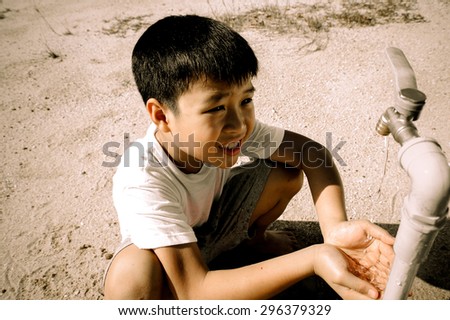 Dark color tone. Close up Asian boy open metal blue water faucet on hot and dry empty land. Water shortage concept.