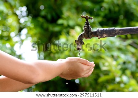 Close up kid hand wait for water drop from old grunge brass faucet on green bokeh from tree background. Water shortage and earth day concept.