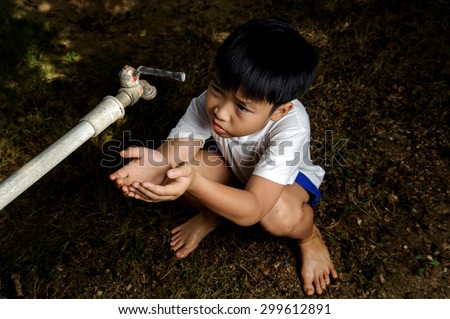 Dark color tone Asian boy waiting for water from faucet on hot and dry empty land. Water shortage concept.