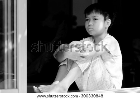 Black and white tone. Asian boy sit beside window after rain at home look sad and lonely concept.