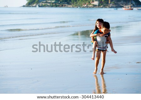 Boy carry his sister at his back on the white sand beach seaside