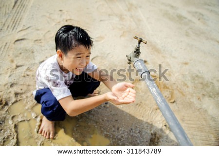 Close up thin focus on old faucet that Young Asian boy waiting for water on hot and dry empty land. Water shortage and drought concept.