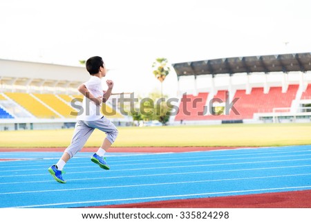 Young Asian boy running on blue track in the stadium during day time to practice himself.