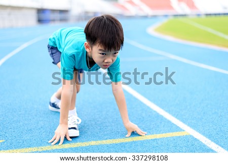 Young Asian boy prepare to start running on blue track in the stadium during day time to practice himself.