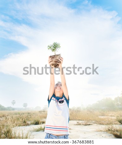 Warm tone, young asian boy lift little plant to the sky. Earth day concept