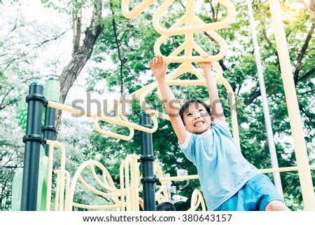 Vintage color tone, Young asian boy hang the yellow bar by his hand to exercise at out door playground under the big tree.