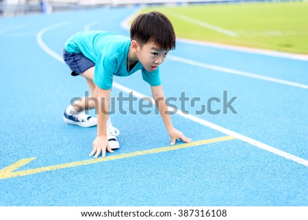 Young Asian boy prepare to start running on blue track in the stadium during day time to practice himself.