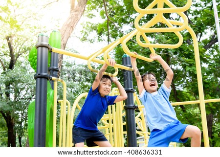 Young asian boy hang the yellow bar by his hand to exercise at out door playground under the big tree.