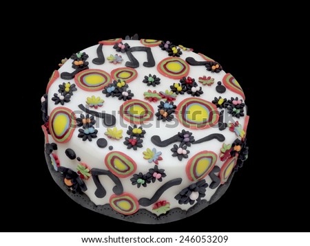 Freshly baked delicious artistic Italian Arts and Crafts cake decorated with music notes and colorful circles on white marzipan icing, high angle view isolated on a dark background