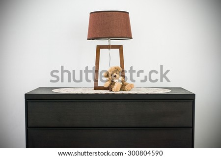 Teddy bear sitting next the urban classic lamp on the black wooden cabinet