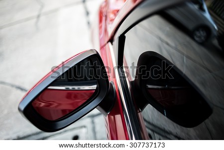 Closeup side rear-view mirror on a modern red car