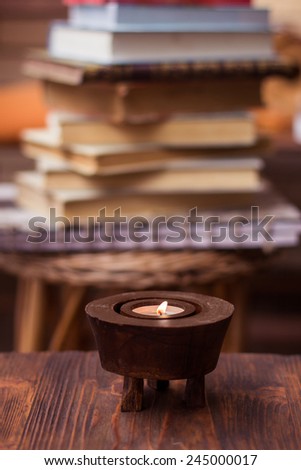 Candle on wooden table with books in background