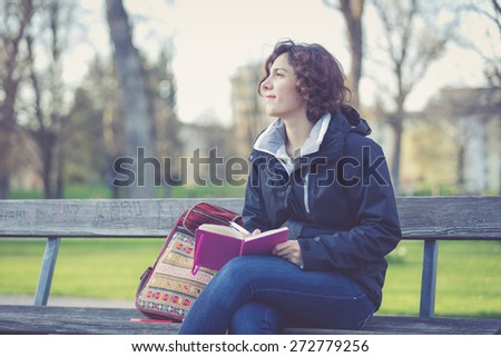 Young girl thinking and writing while sitting on a bench at park.