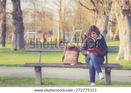 young girl sitting on a bench at park and reading E-book