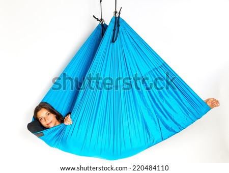 Young woman lying in a blue hammock for anti-gravity aerial yoga exercise on a seamless white background.