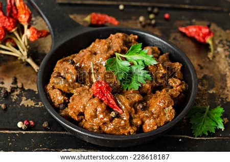 Stewed beef liver with tomatoes sauce in iron pot on iron dark background