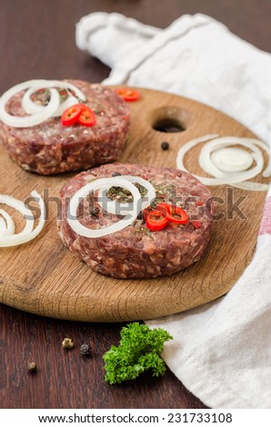 Raw burger cutlets with onion, peppers and parsley  on wooden plate and wooden background